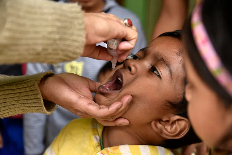 child has mouth open and receives drops from adult hands