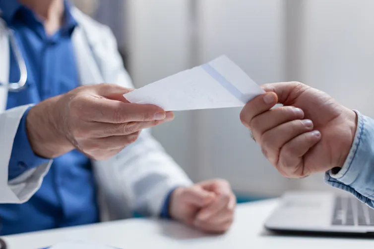 Doctor hands patient a sheet of paper.