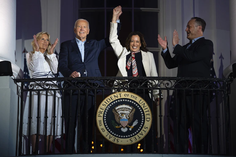 Kamala Harris waves from a balcony, with her hand held aloft by Joe Biden
