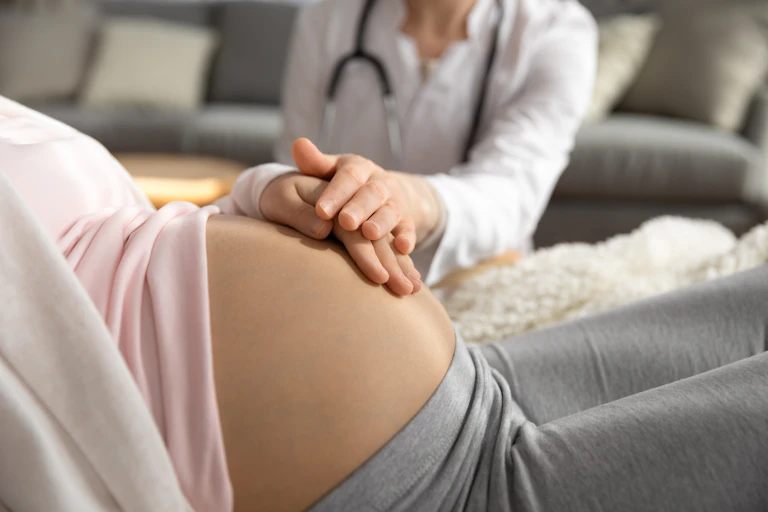 A doctor presses their hand on a pregnant woman's stomach.