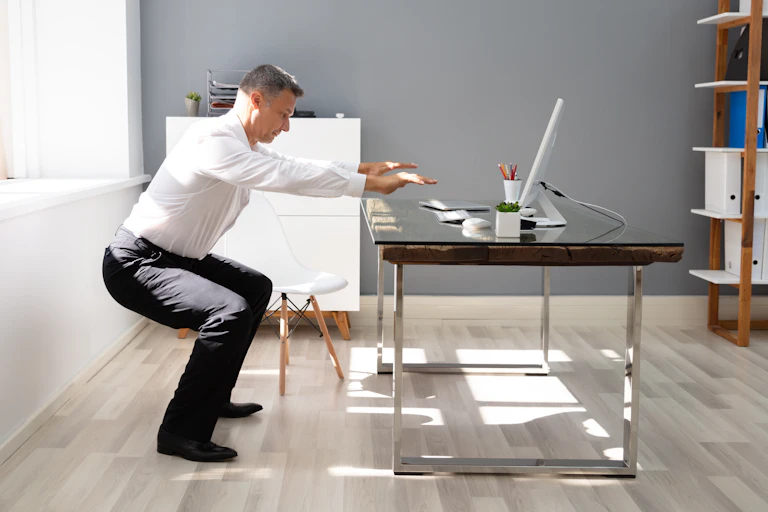 Man in business attire squatting next to desk