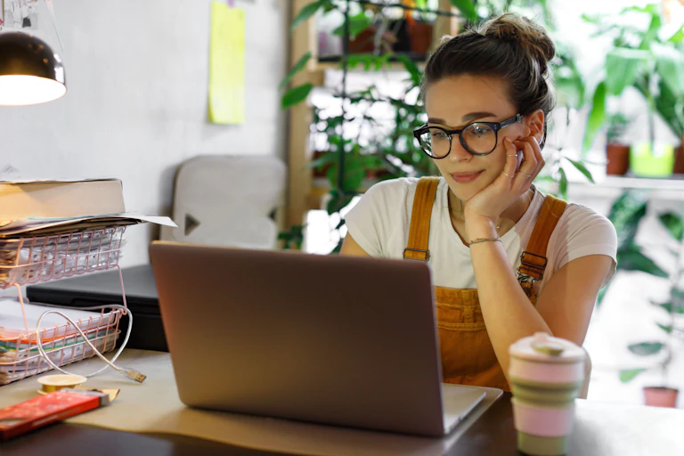Young woman sitting at home at desk looking at laptop