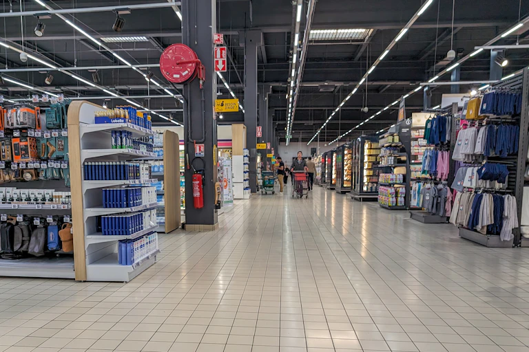 rayons d'un hypermarché avec au loin une personne qui pousse un chariot dans un magasin vide
