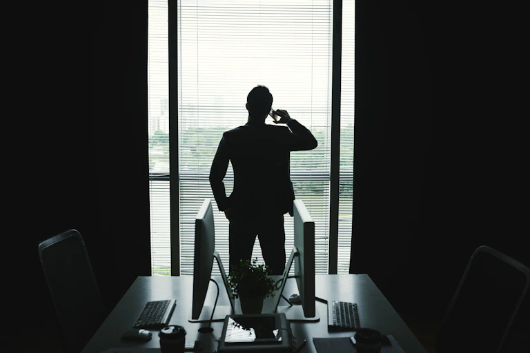 Silhouette of a man in a business suit talking on the phone in an office in front of an open window