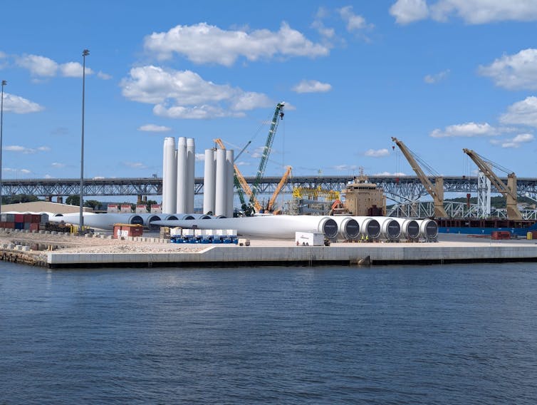 A pier with cranes and huge wind turbine blades, seen from the water