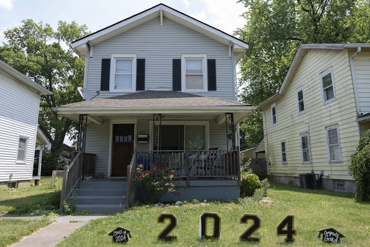 A two-story house with a small, neatly mown lawn, and numbers signs spelling out '2024' in the yard.