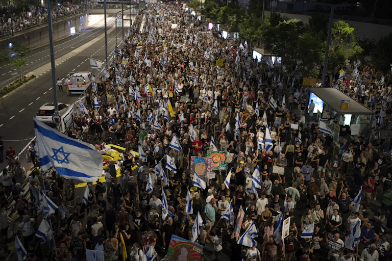 Hundreds of people carrying Israeli flags walk through street at night