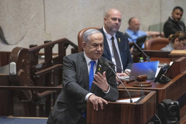 a white man in a gray suit gestures as he speaks at a lectern