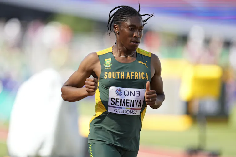 A muscular Black woman in a green and yellow tank top runs a track