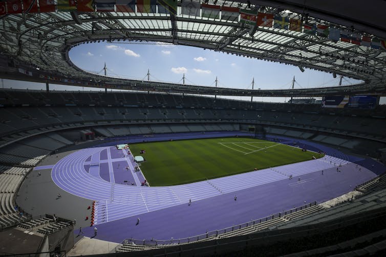 A stadium with an open roof showing a bright blue track and green field below.