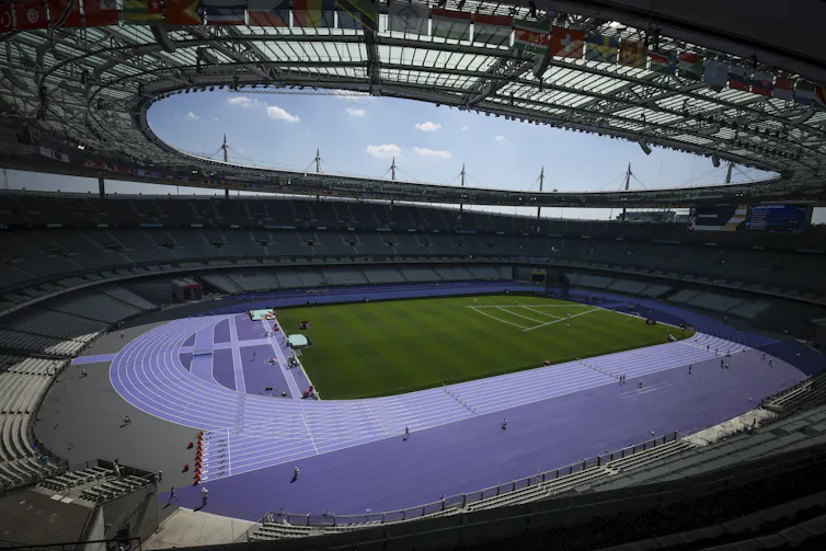 A stadium with an open roof showing a bright blue track and green field below.
