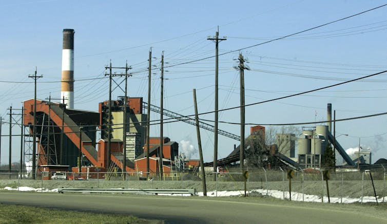 A rusty red industrial structure and telephone poles against an empty blue sky.