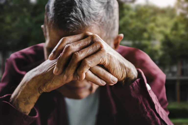 older man holds face in hands