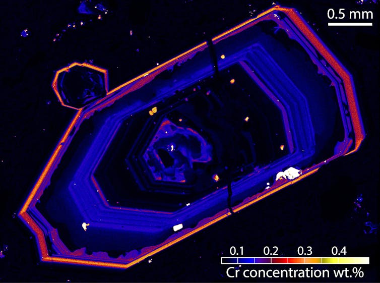 Microscope image of a blueish crystal outlined in yellow-red.