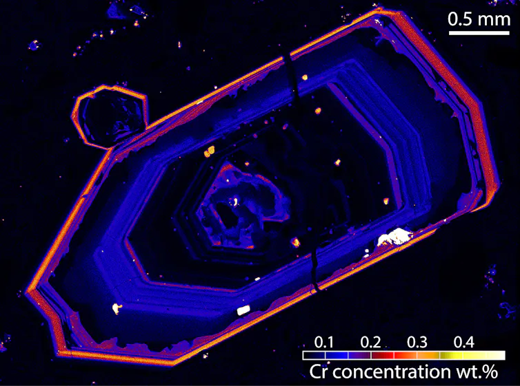 Microscope image of a blueish crystal outlined in yellow-red.