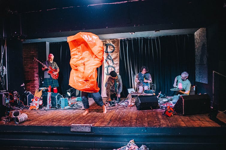 A group of Dadaist performers on stage, one with an orange bag over their head.