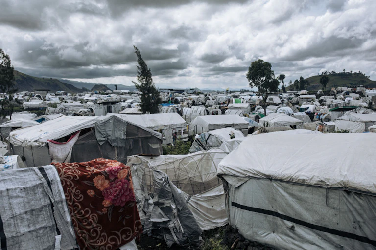 A camp of low-lying white tarpo temporary shelters of all shapes and sizes stretch back as far as the eye can see.
