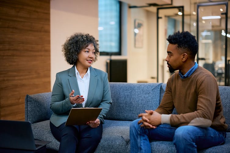 A young man talks to a woman while both are seated on a couch