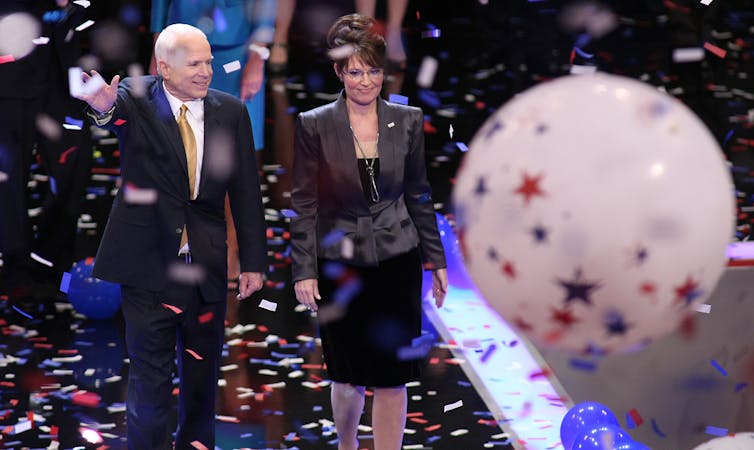A man and a woman on a stage with confetti raining down and balloons.