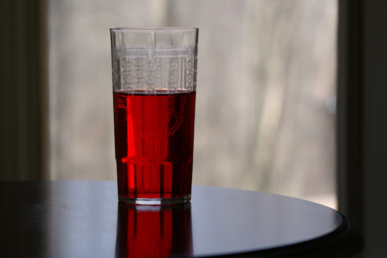 glass of cranberry juice sits on table in darkened room
