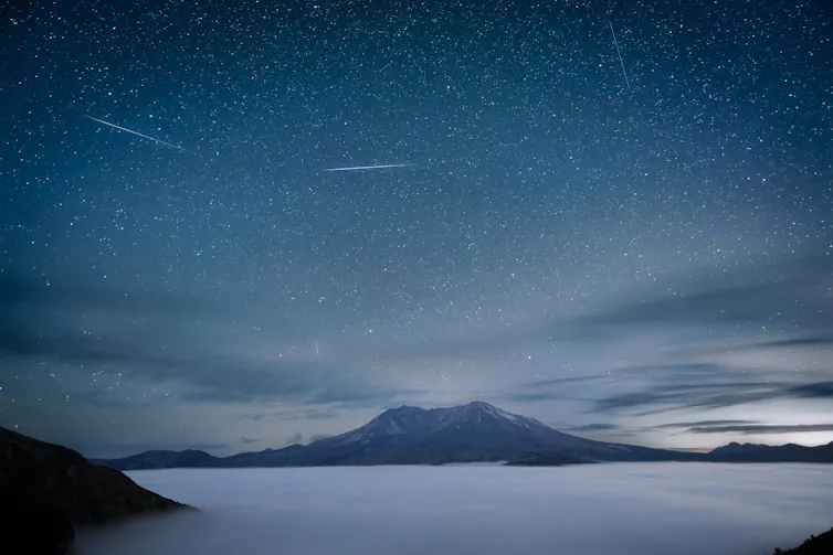 A misty mountain in the distance with a foggy lake in the foreground and several bright streaks in the sky.