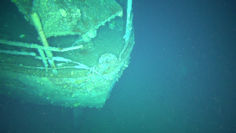 A blue and green underwater image of a deeply encrusted front of a ship.