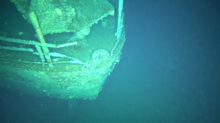 A blue and green underwater image of a deeply encrusted front of a ship.
