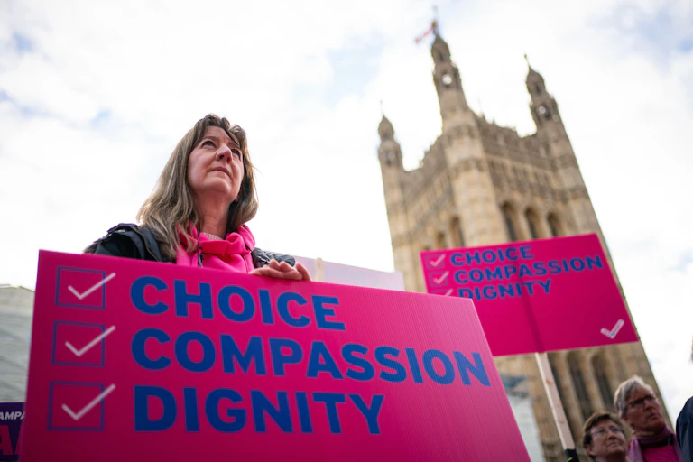 A woman holding a sign reading 'choice, compassion, dignity' outside Westminster.