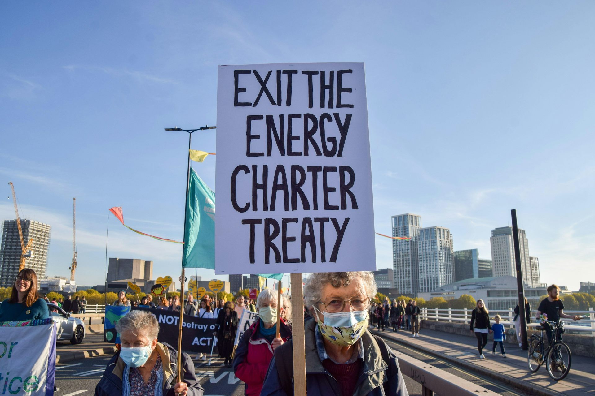 A woman holds up a sign that says Exit the Energy Charter Treaty. 