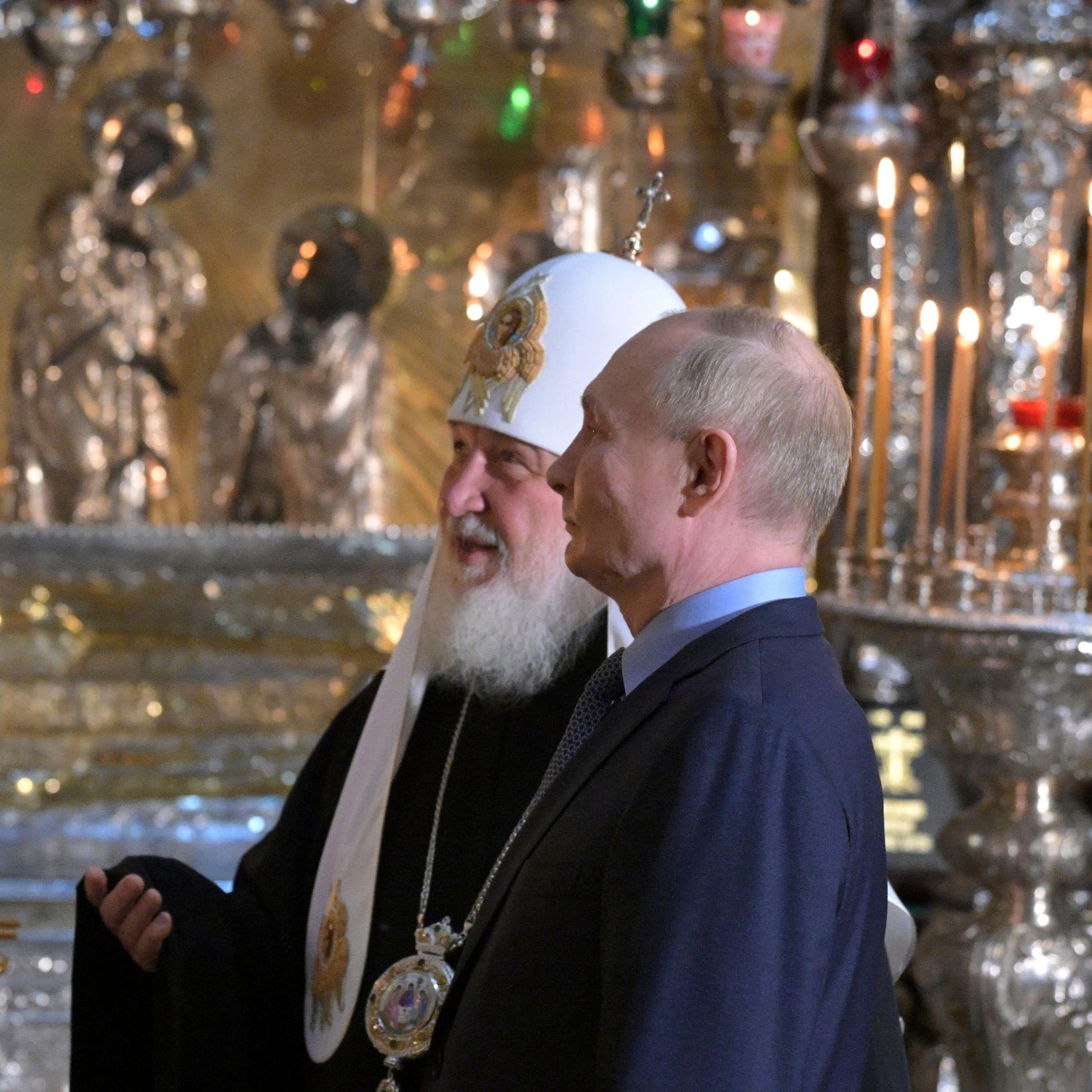 Russian president Vladimir Putin, right, accompanied by Russian Orthodox Patriarch Kirill visits to the Trinity Cathedral otuside Moscow. They are standing talking to each other.