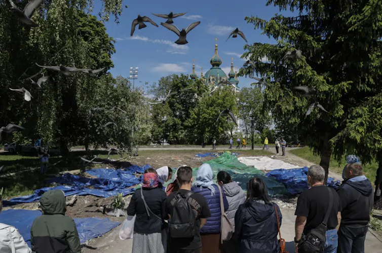 Orthodox believers pray near the debris of their chapel in downtown Kyiv. Debris is spread out in front of them.