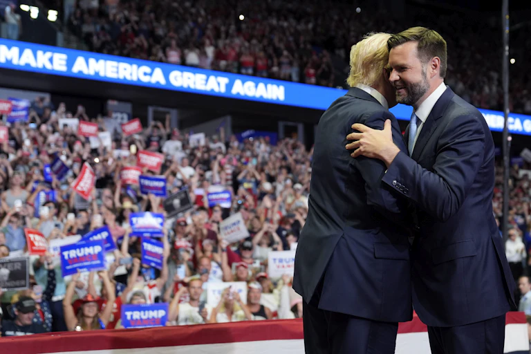 Trump and Vance embrace onstage in fromt of a crowd waving signs