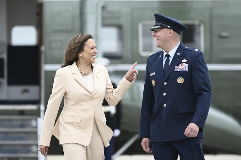 A woman with dark hair in a cream suit laughs with a man in an Air Force uniform.