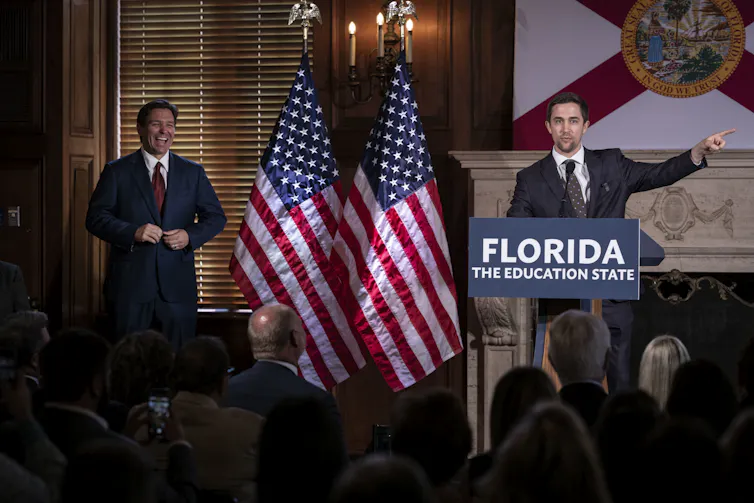 A man speaks at a lectern while a man to his right listens.
