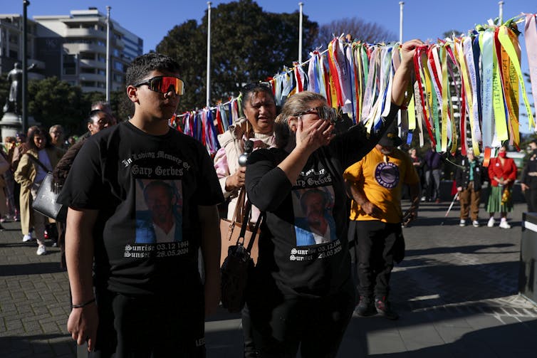 People, one crying, with colourful tags representing survivors of abuse in state care.