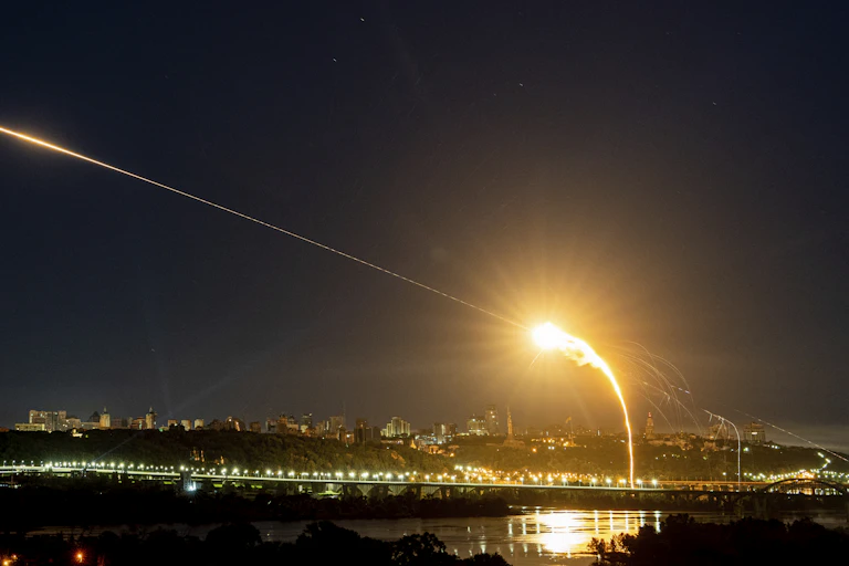 A night-time photo showing a beam of light and an explosion over a city.