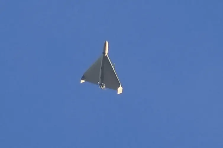 A mostly triangular grey flying object in a blue sky.