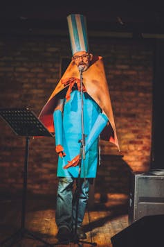 A man dressed in a strange Dada costume performing on stage.