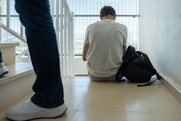 Boy sitting with bag on stairs with back to camera