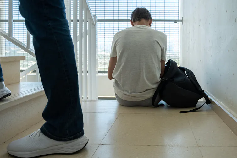 Boy sitting with bag on stairs with back to camera