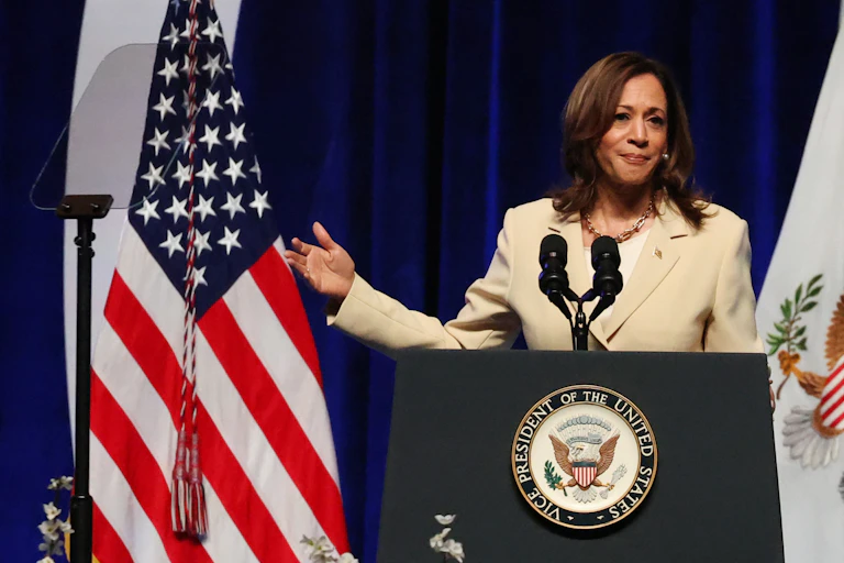 US vice-president Kamala Harris stadns at a podium gesturing towards an American flag.