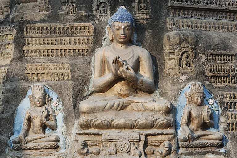 A large stone statue of the Buddha, with two smaller statues next to him. In the background are rows of tiny statues.