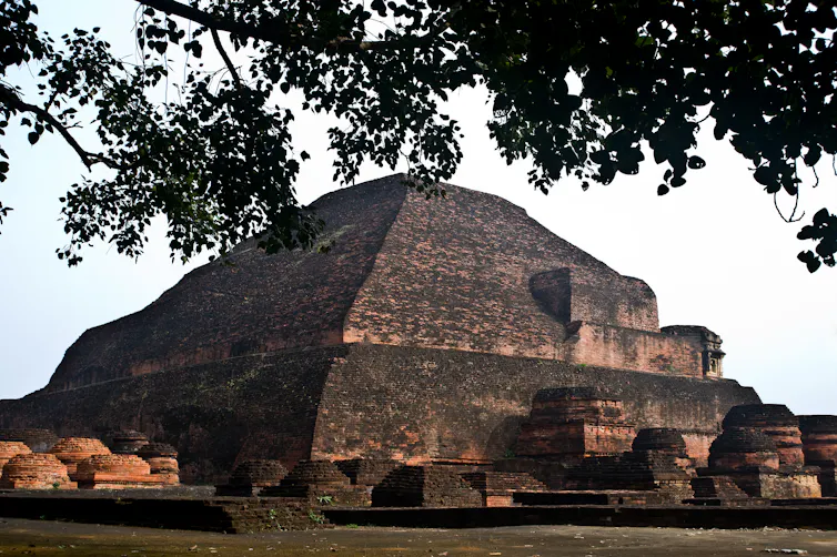 A large mound-like ancient stone structure, which appears blackened over the years, with a large tree near it.