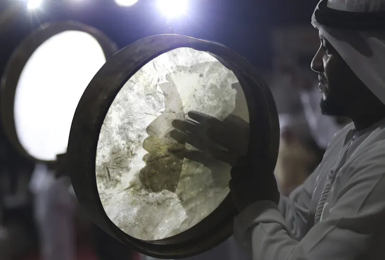 A man wearing a white headdress playing a drum.