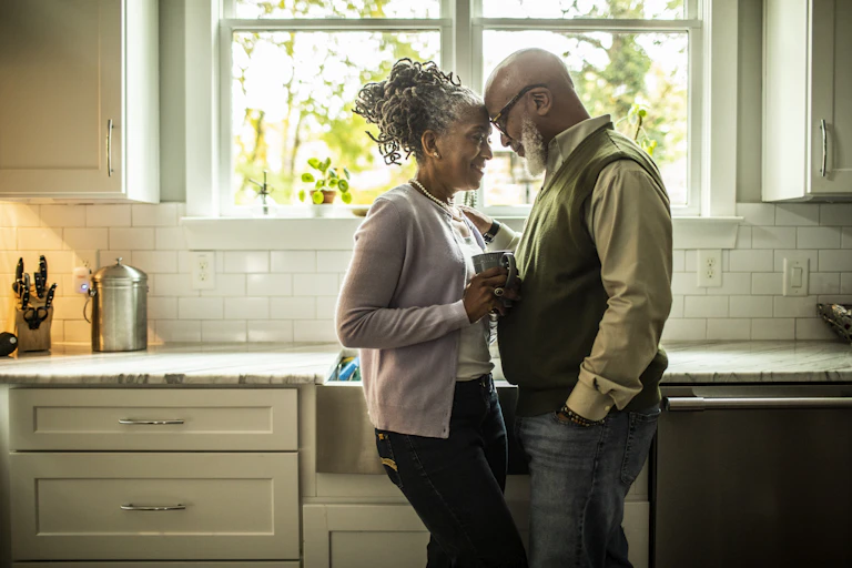 Older couple standing close together in kitchen, heads touching