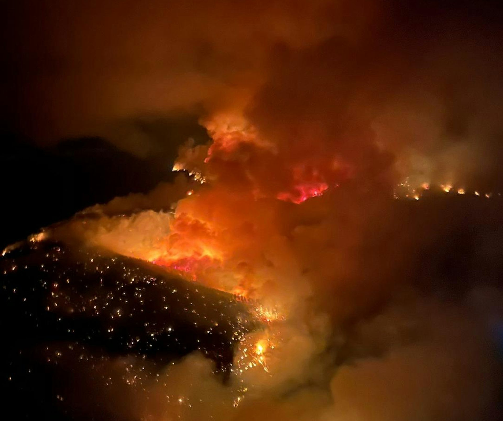 Smoke blankets a landscape with a glowing wildfire seen at night