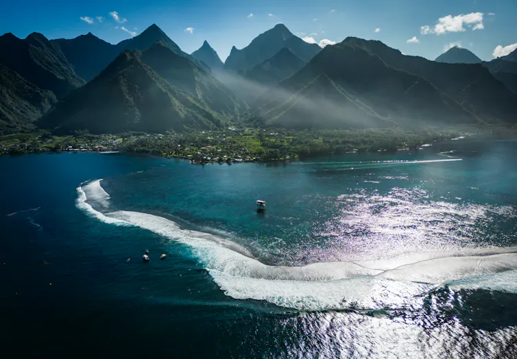 Tahiti Iti coast viewed from above and out to sea showing mountain peaks, water craft and surfers