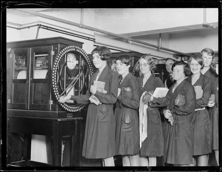 A line of women at a complicated machine.