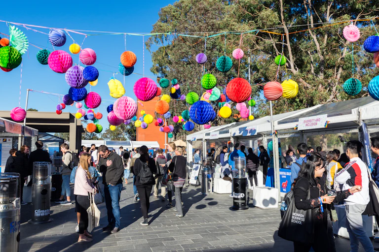 Young people walk among outdoor stalls. Paper decorations hang above them.
