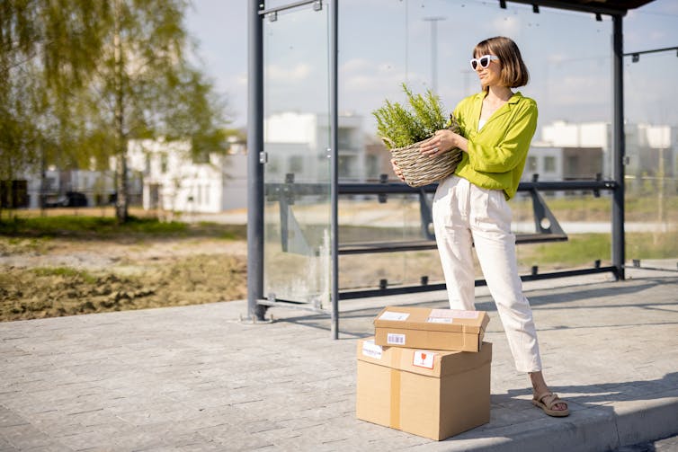 A young woman with a couple of packages waits at a bus stop